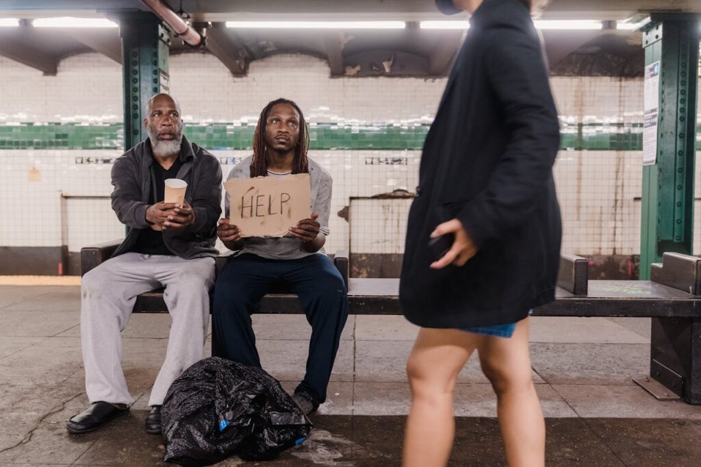 Two men seeking help at a subway platform, highlighting urban poverty and social issues.