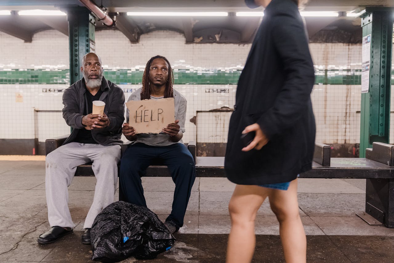 Two men seeking help at a subway platform, highlighting urban poverty and social issues.